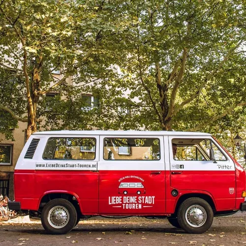 Roter Oldtimer-Bulli „Pitter“ der Liebe Deine Stadt-Touren, geparkt unter Bäumen vor einem Café