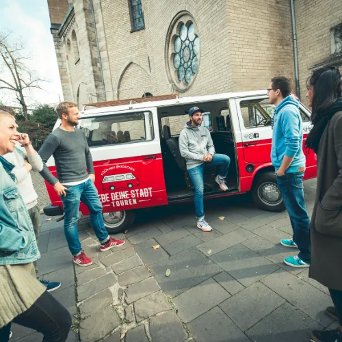 Tourgruppe steht mit Kölsch am geöffneten Bulli vor einer Kölner Kirche