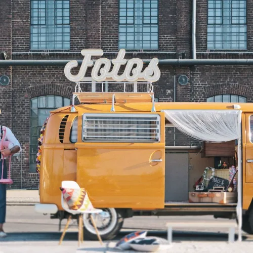 Brautpaar mit dem orangefarbenen Fotobulli vor einer Backsteinhalle