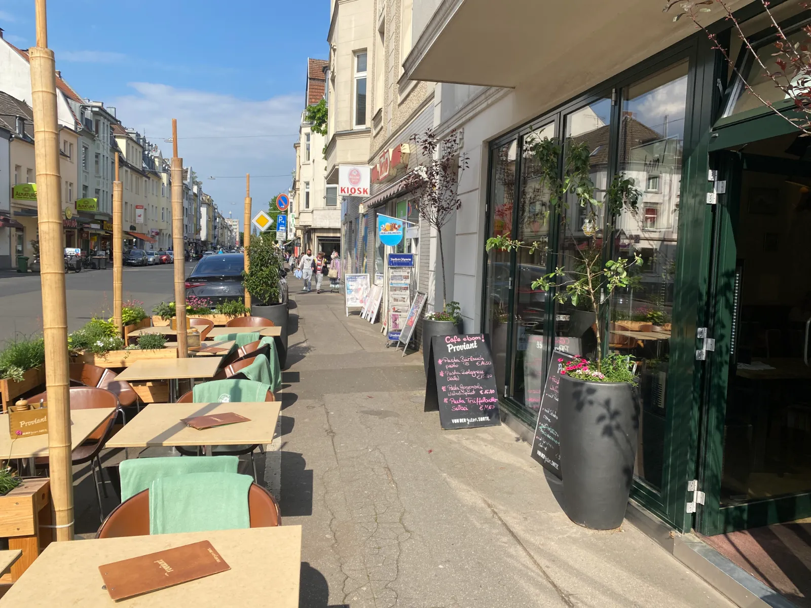 Gedeckte Tische eines Cafés auf dem Gehweg einer belebten Einkaufsstraße, Station einer kulinarischen Gusto-Route