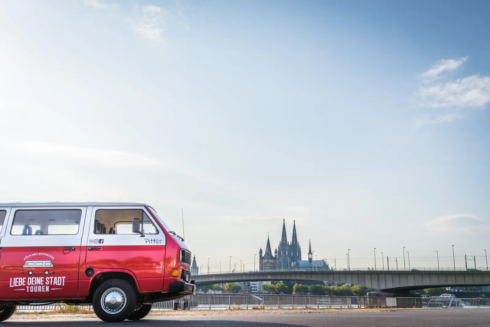 Roter Oldtimer-Bulli der Liebe Deine Stadt-Touren am Rheinufer vor dem Kölner Dom