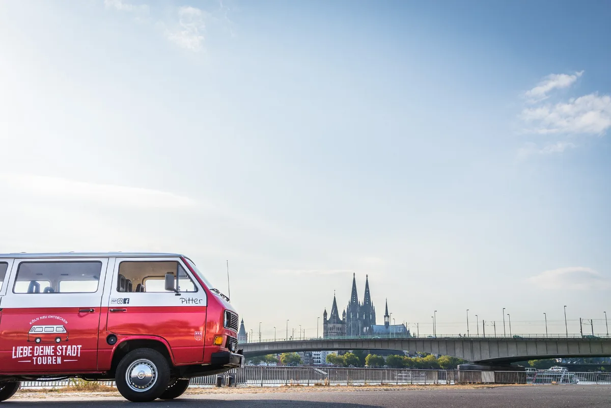 Roter Oldtimer-Bulli der Liebe Deine Stadt-Touren am Rheinufer vor dem Kölner Dom